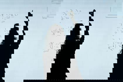 Silhouette of a person writing maths formulae on a whiteboard
