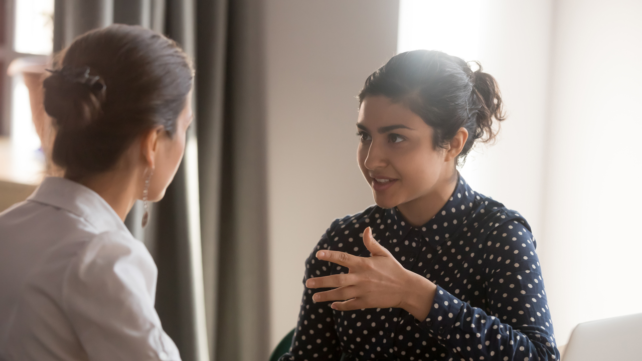 Two people in discussion, facing each other. One has their back turned to the camera. 