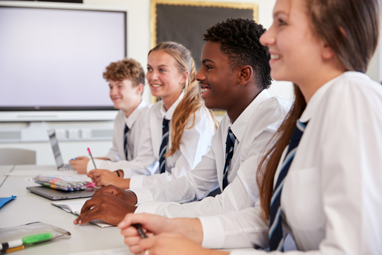 A group of four students sat at a classroom desk looking happy