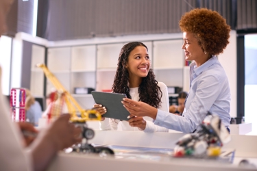 Female secondary school teacher with digital tablet helping girl in technology lesson