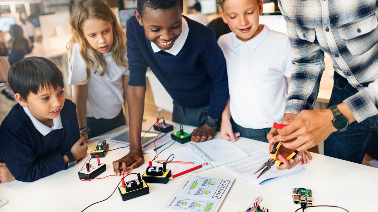 Four students and a teacher working at a bench learning about electricity