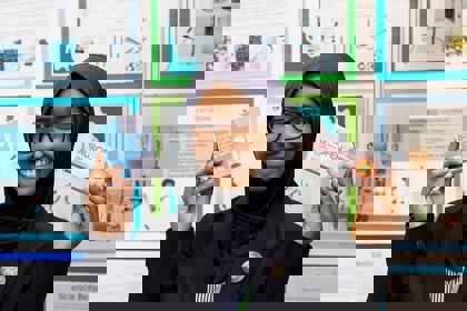 The Big Bang Competition's UK Young Scientist of the Year winner stands and smiles at the camera surrounded by her working boards and sketches that show how her winning idea developed