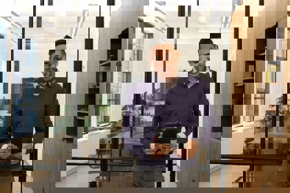 A young person stands in an office in front of an empty boardroom. They smile and look at the screen in their hands.