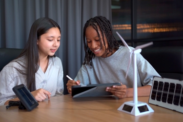 Two young people study a screen. A wind turbine is on the table between them.