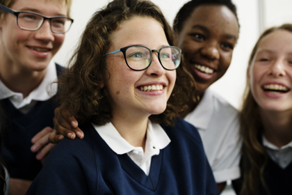 Four school students stand close together as they smile