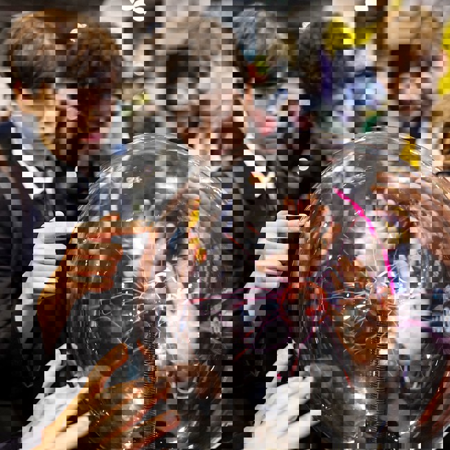 Six hands touch a plasma ball on display at The Big Bang Fair. Four young people are watching the effects.