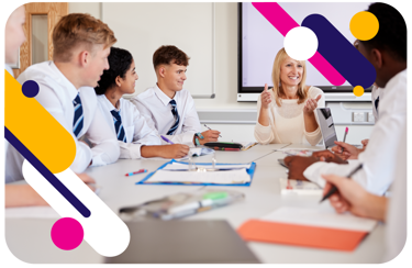Teacher and a group of young people sit around a large table. They have pens and note books, working as the teacher talks.