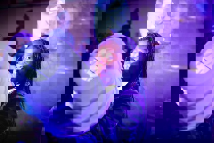 A young person at The Big Bang Fair is lit by theatrical lighting. They are holding a piece of equipment which is glowing. They stare into the foreground.