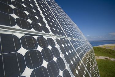 A close up of a large solar panel. In the distance there is landscape and blue sky.