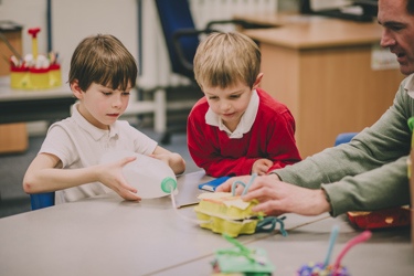 Primary school aged children in a classroom at a table with their teacher doing a practical science experiment