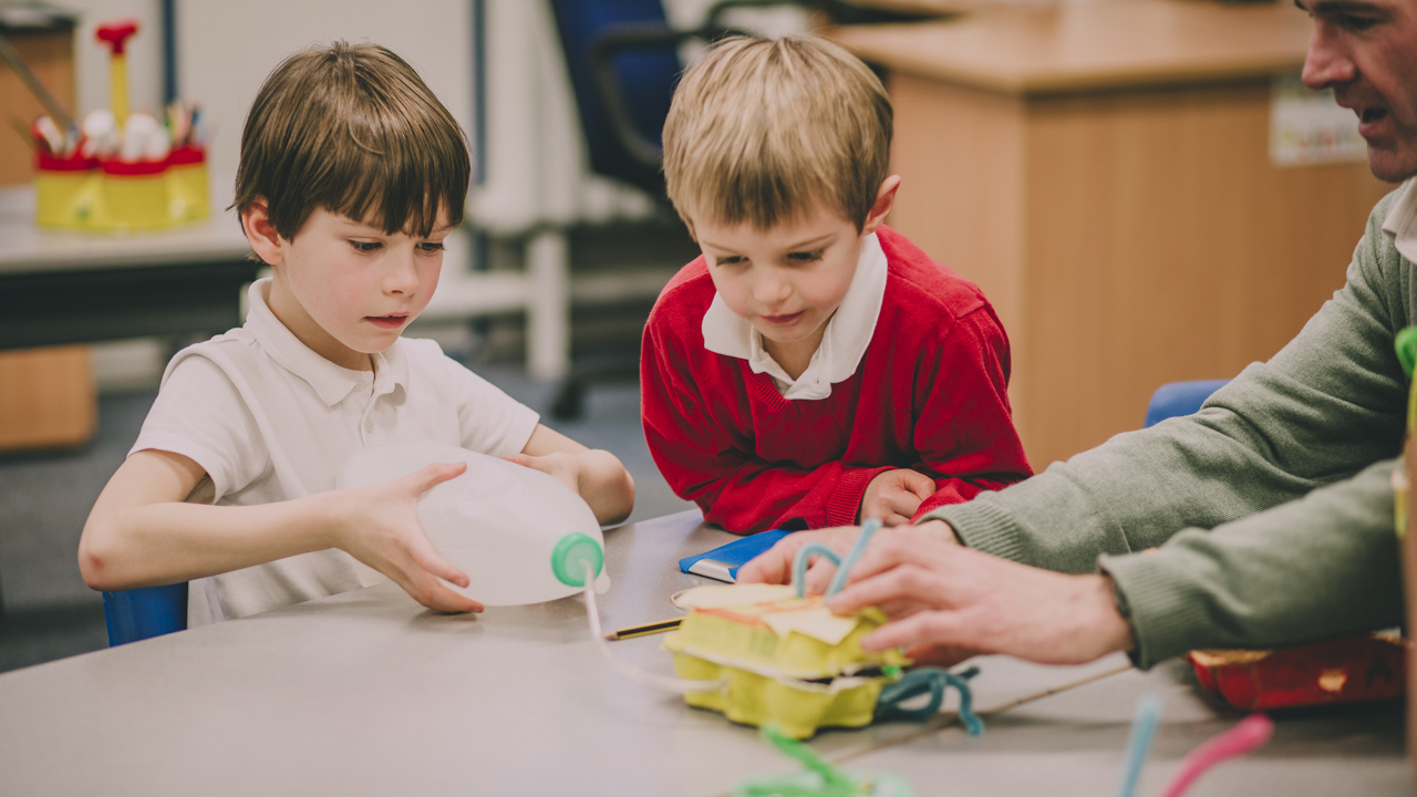 Primary school aged children in a classroom at a table with their teacher doing a practical science experiment