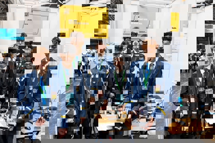 The six winners of The Big Bang Competition UK Young Technologists of the Year stand in an exhibition area displaying a model of their product along with sketches and working drawings to show how their idea developed. They all face the camera