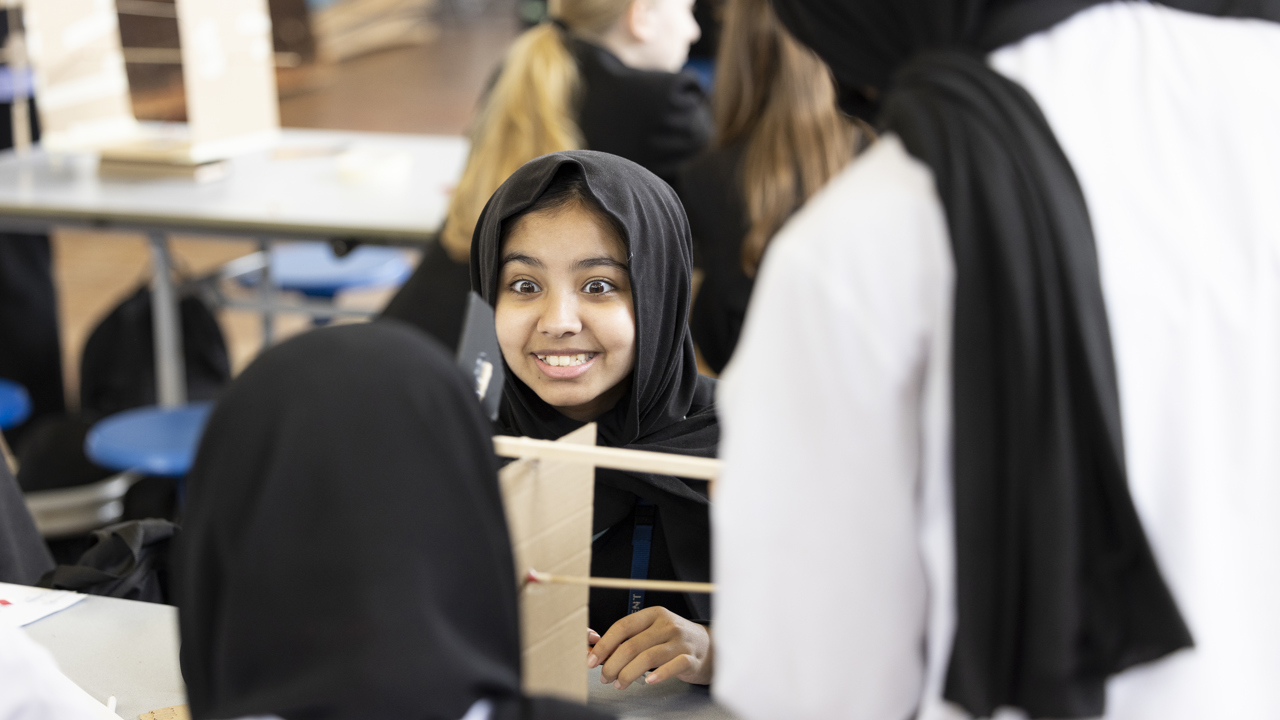 Close up of young person working on a cardboard model during a science lesson. There are other students in the room